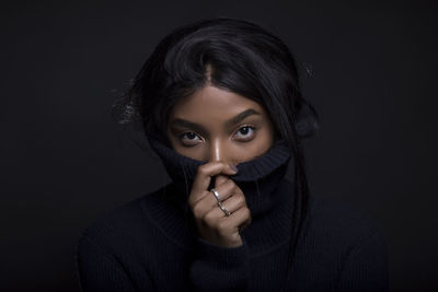 Portrait of beautiful woman covering face with sweater against black background