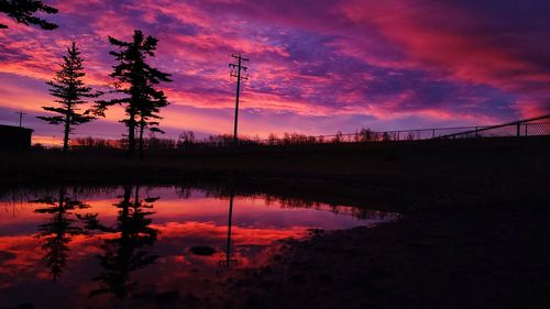 Silhouette trees by lake against dramatic sky during sunset