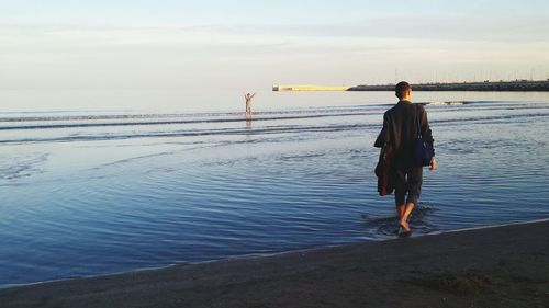 Rear view of man standing on beach against sky