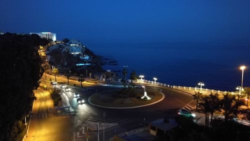 High angle view of illuminated city by sea at night