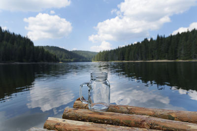 Jar on logs floating over lake against cloudy sky