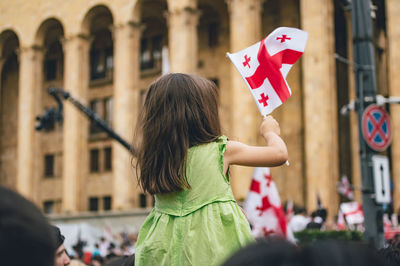 Rear view of woman standing against wall in city