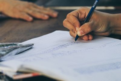 Cropped hand writing in book at table