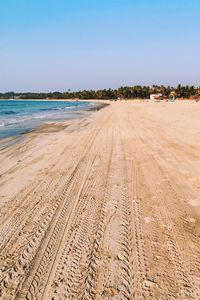 Tire tracks on beach against clear sky