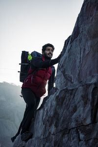 Young indian climber and traveler climbing up the mountain rock during sunset. 