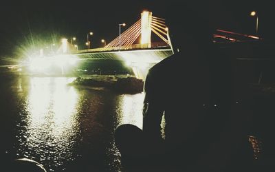 Man in illuminated city by river against sky at night