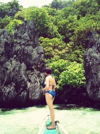 Rear view of woman standing on rock against trees