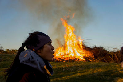 Optical illusion of woman blowing burning fire on field against sky