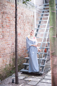 Portrait of smiling young woman standing against brick wall