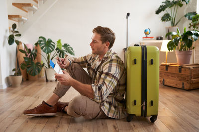 Side view of man sitting on suitcase at home