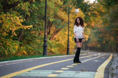 Woman standing on road amidst trees during autumn