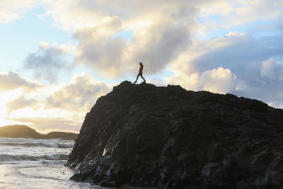 Man standing on rock by sea against sky