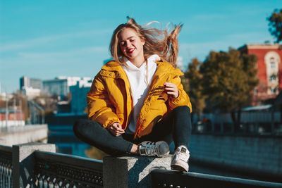 Young woman smiling while sitting against built structure