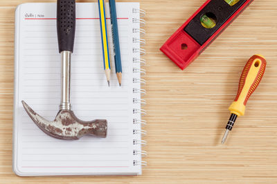 High angle view of book and pencils with hammer on table