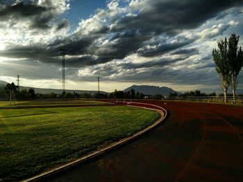 Road passing through field against cloudy sky