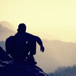 Tired hiker with sporty backpack sit on rocky peak and watching into spring daybreak mist  