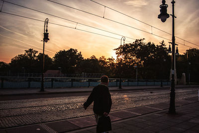 Rear view of man walking at railroad station platform during sunset