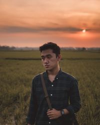 Young man standing on field against sky during sunset