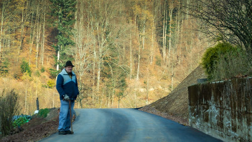 Man standing on road amidst trees in forest