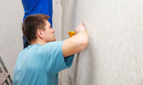 Side view of painter putting wallpaper on wall at construction site