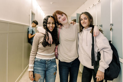 Portrait of smiling teenage girls standing in school corridor