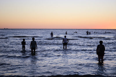 Silhouette people on beach against sky during sunset