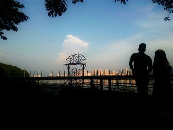 Silhouette people at amusement park against sky