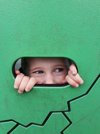 Boy looking away while peeking through hole