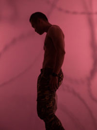 Side view of shirtless young man standing against red textile