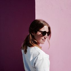 Smiling woman wearing sunglasses while standing against pink wall