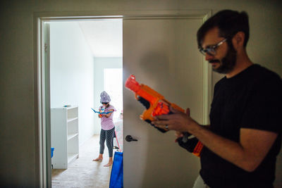 Father and daughter playing with toy guns at doorway