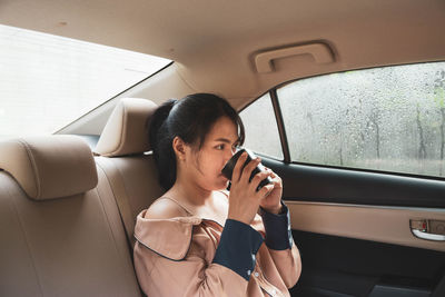 Side view of woman drinking coffee while sitting in car