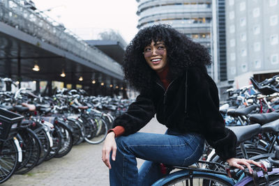 Smiling young woman sitting on bicycle at parking station