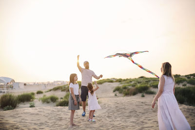 Father flying kite with kids during sunset