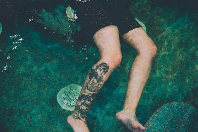 Low section of man with tattoo on leg swimming in pool