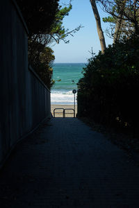 Empty footpath by sea against sky