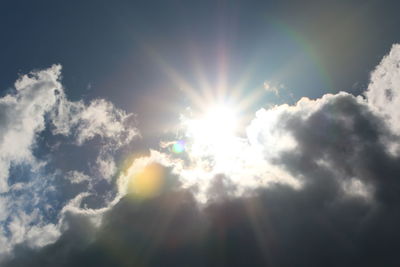 Low angle view of sunlight streaming through clouds