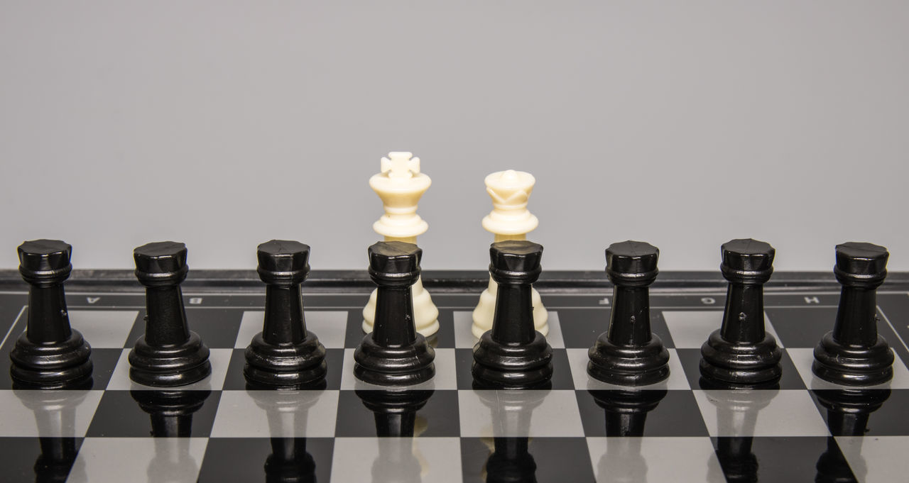 LOW ANGLE VIEW OF CHESS PIECES ON BOARD AGAINST WHITE BACKGROUND