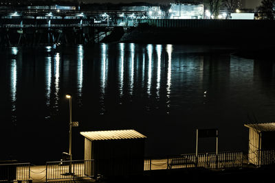 Illuminated building by lake against sky at night