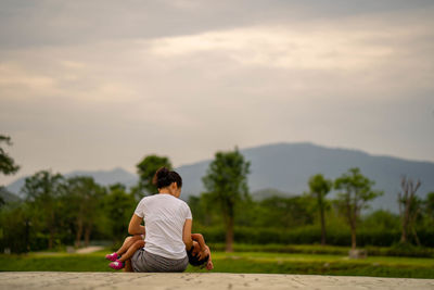 Rear view of mother with daughter sitting against landscape