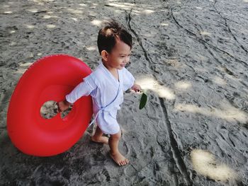 High angle view of boy with red inflatable ring walking on sand at beach