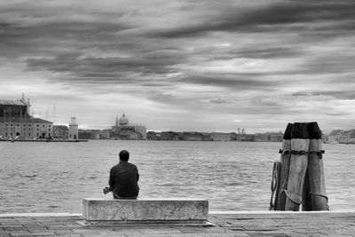 Rear view of man sitting on bridge against sky