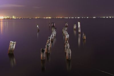 Damaged wooden posts in sea against sky at night