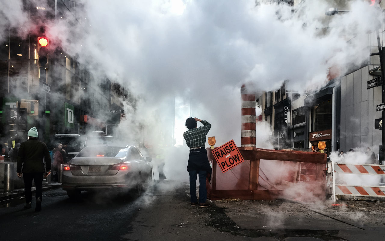 transportation, weather, men, building exterior, mode of transport, street, smoke - physical structure, land vehicle, sky, cloud - sky, built structure, lifestyles, architecture, car, road, rear view, city, full length