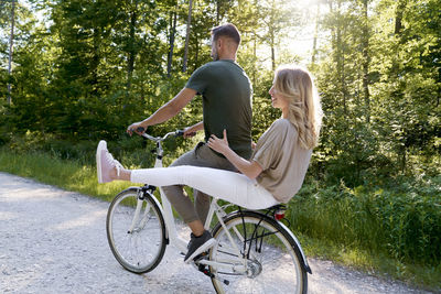 Happy couple sitting on bicycle against trees