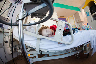 Curly-haired toddler sleeps alone in large hospital bed.