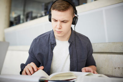 Young student wearing headphones while studying at table in university