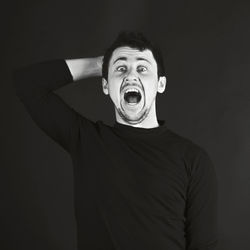 Portrait of man shouting while standing against black background