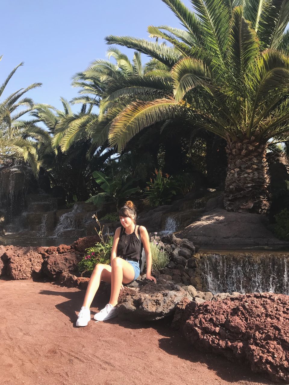 real people, rock - object, palm tree, young women, leisure activity, young adult, rock formation, full length, tree, one person, lifestyles, day, casual clothing, happiness, outdoors, beautiful woman, sitting, nature, water, beauty in nature, sky