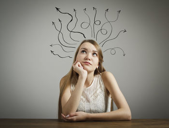 Portrait of young woman looking away while sitting on table against wall